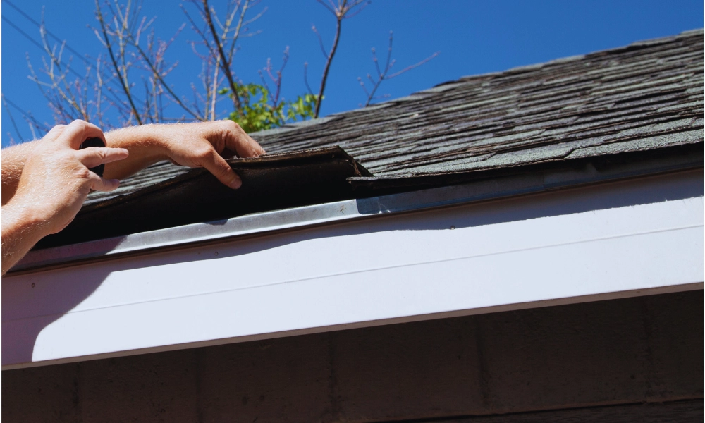 An inspector looking at the edge of a shingle roof.